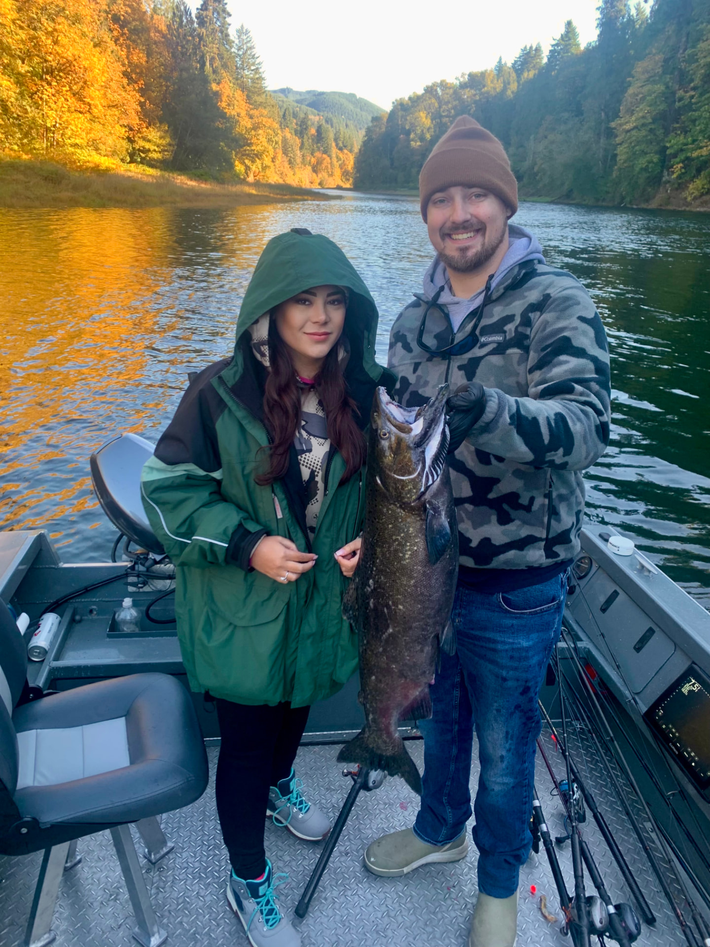 Two guests holding a big fall Chinook salmon aboard the jet sled on a river lined with golden autumn trees